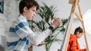 A Boy Holding a Paint Brush While Painting on the Canvas