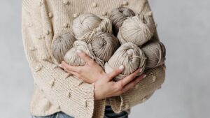A Person in Beige Knitted Sweater Holding Yarns