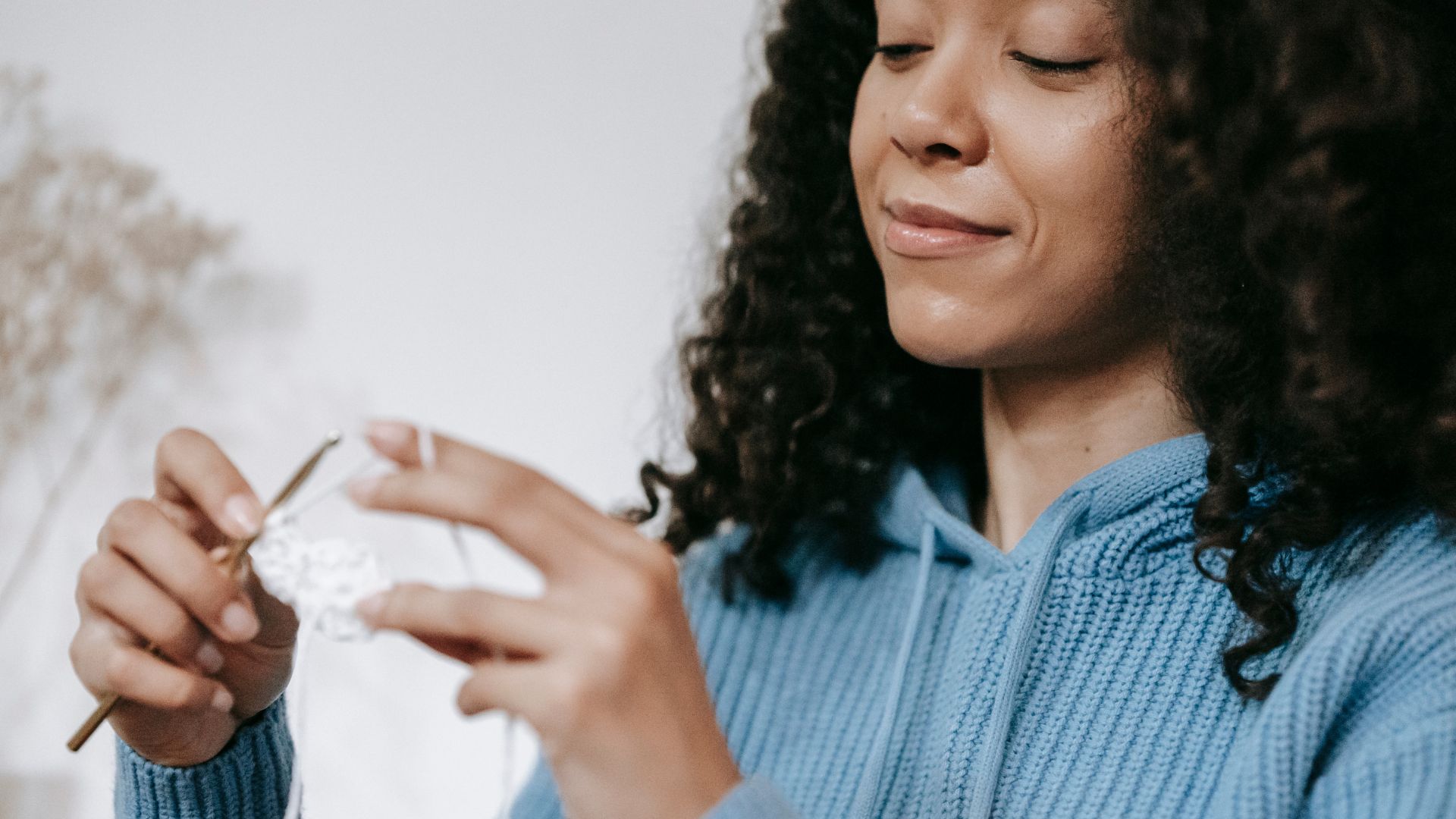 A Smiling Woman in Knitted Sweater Holding a Crochet Hook and Yarn