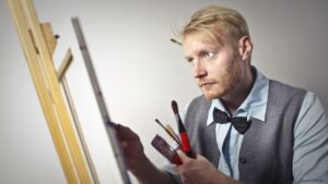 Calm male artist painting on canvas using paintbrushes