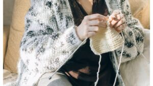 Elderly Woman in White and Black Cardigan Sitting on a Couch Doing Crochet