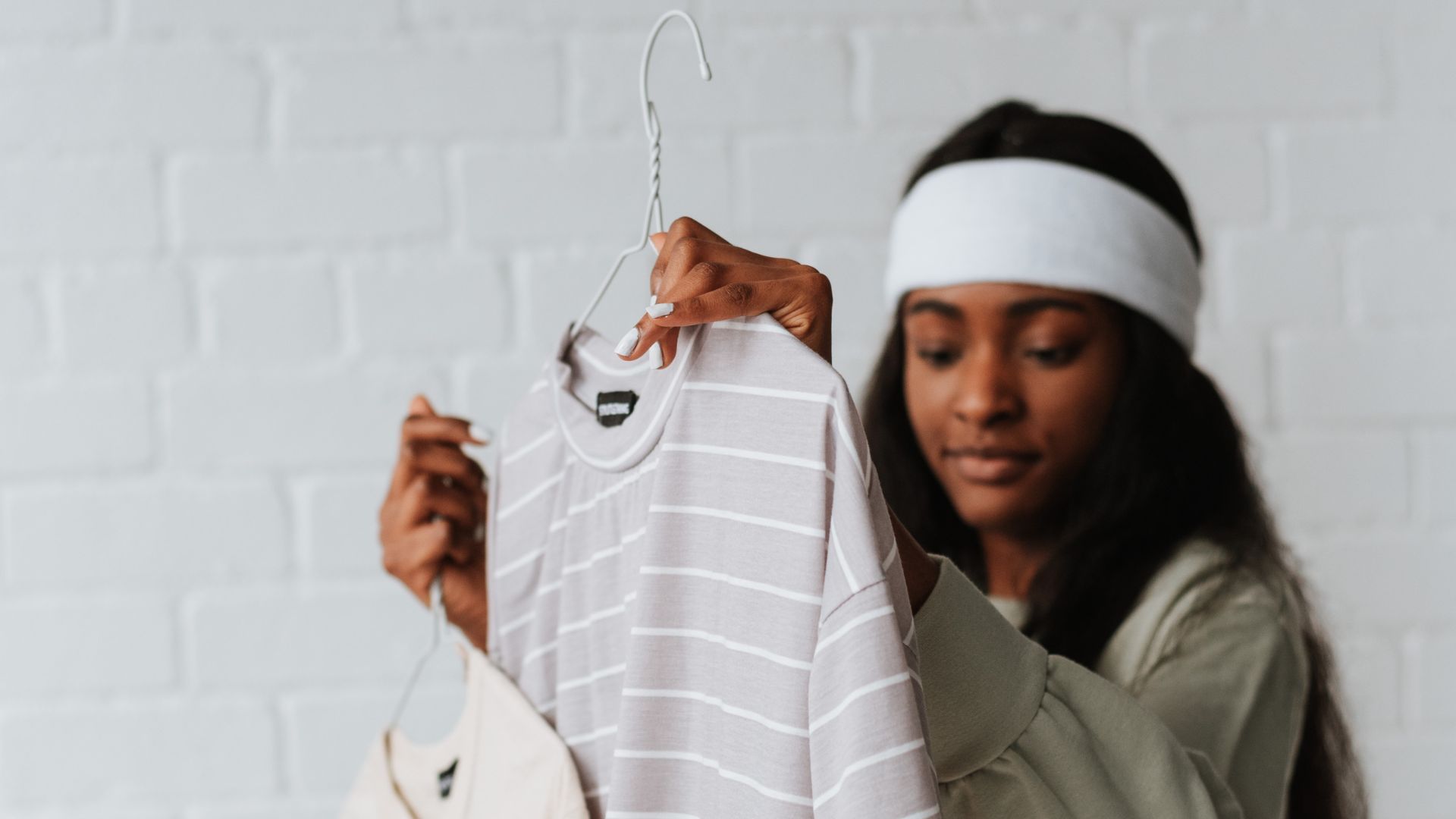 Ethnic woman choosing t shirts on hangers on white background