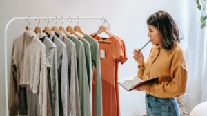 Pensive ethnic designer with agenda against rack with various wear