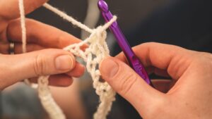 Person Holding Purple Crochet Hook and White Yarn