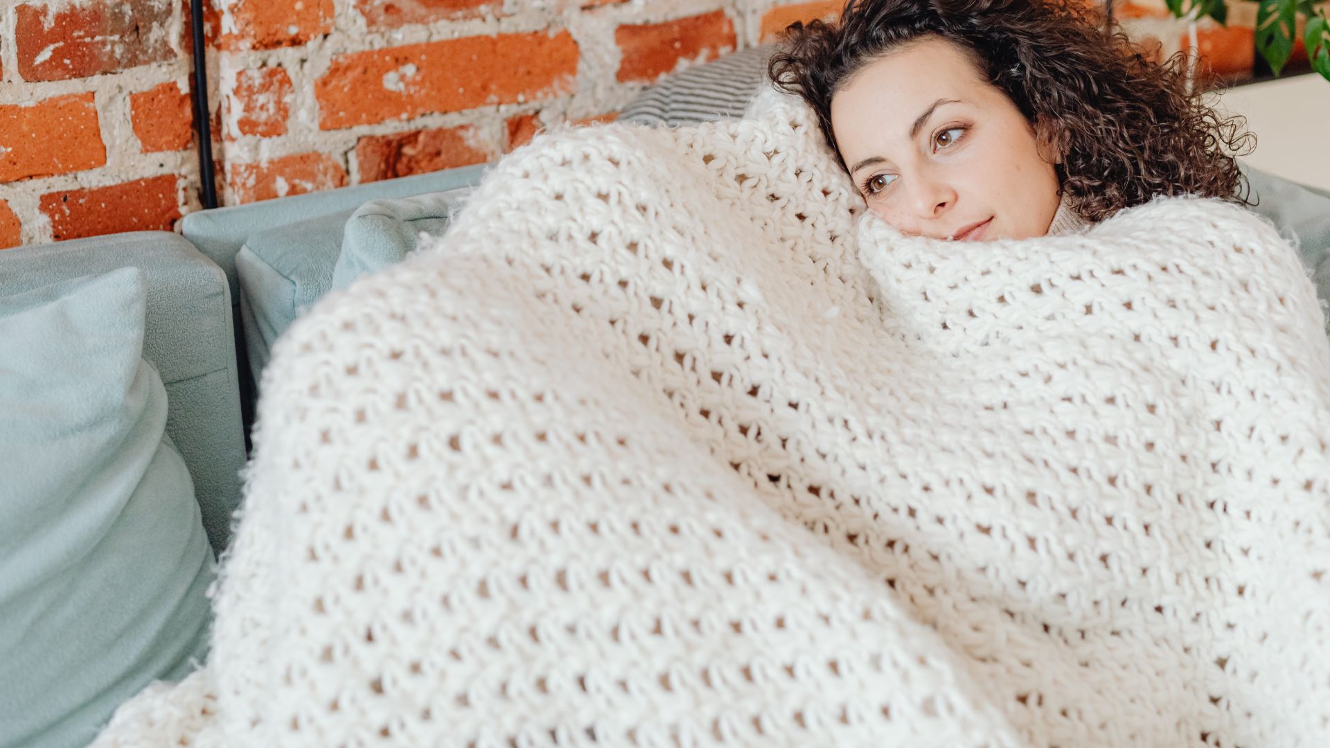 Woman Lying on a Couch Covered with Crochet Blanket while Looking Afar