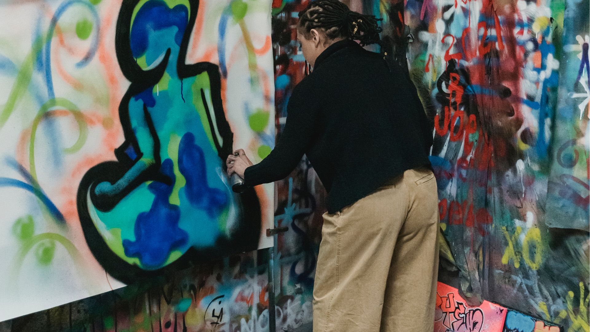 Woman in Black Shirt and Brown Pants Standing Beside Wall With Graffiti